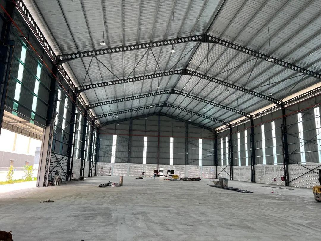 A wide, empty clear-span factory hall with a steel roof and daylight panels along both walls